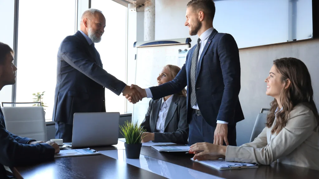 photo of two business people shaking hands while other business people look on representing Edison Electric Institute choosing GlobalMeet as their virtual events platform