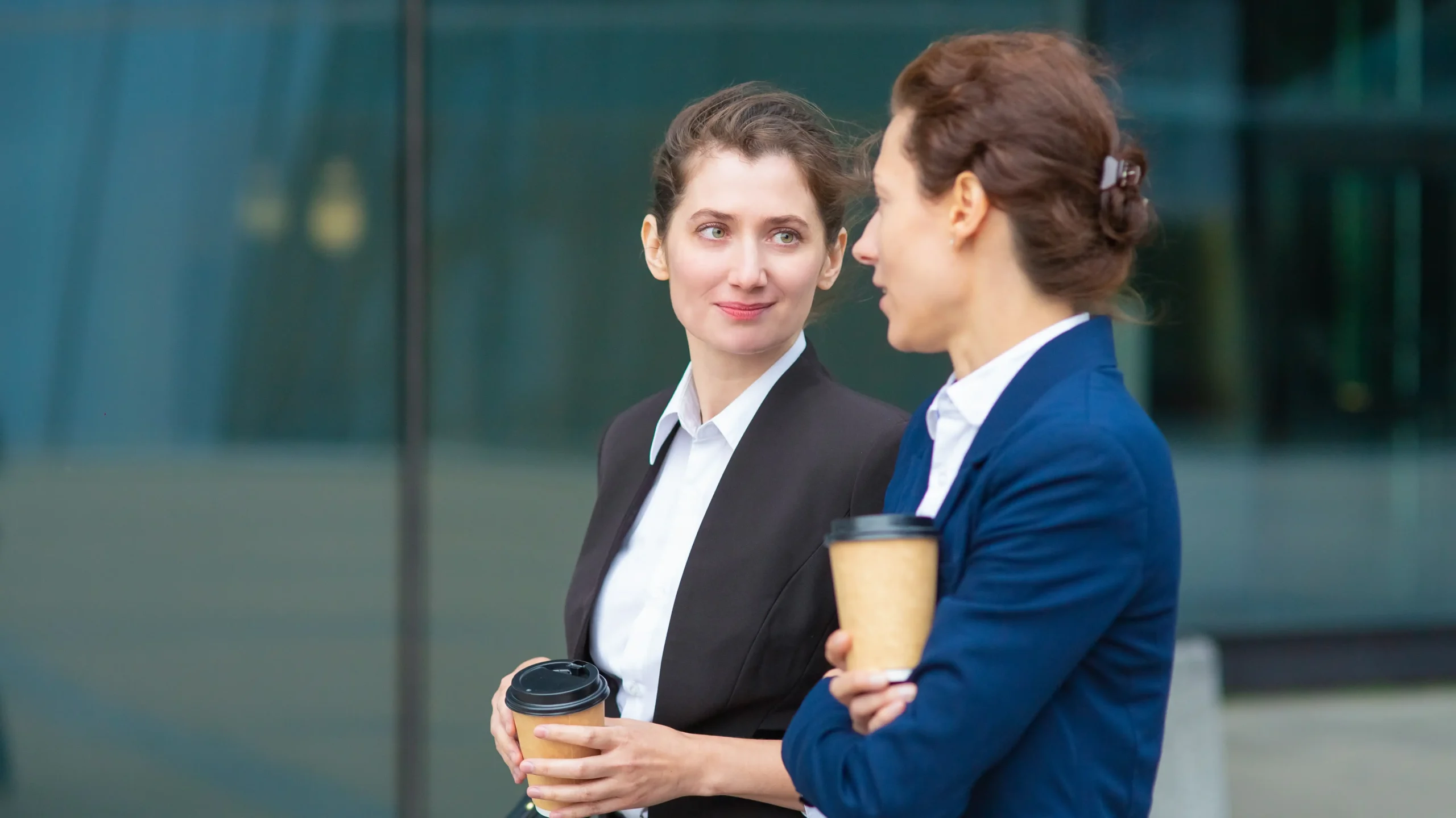 two women in business attire walk outside with coffees in their hands talking about video for wealth management with globalmeet's virtual event platform